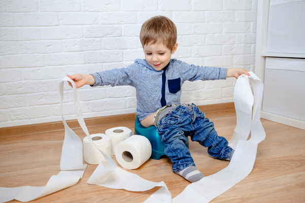 Boy sitting on a potty playing with rolls of toilet paper