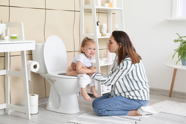 Girl crying whilst sitting on toilet with her mother kneeling beside her