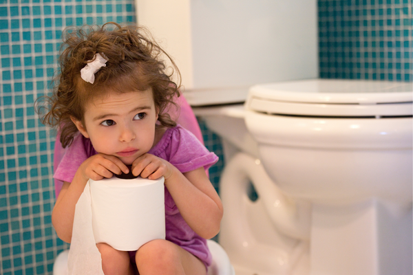 Girl sitting with toilet paper in her lap next to a toilet looking shy