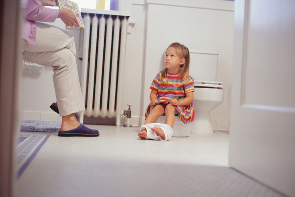 Girl sitting on a potty in a bathroom with her mom next to her
