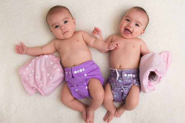 Twin babies laying next to each other wearing cloth diapers