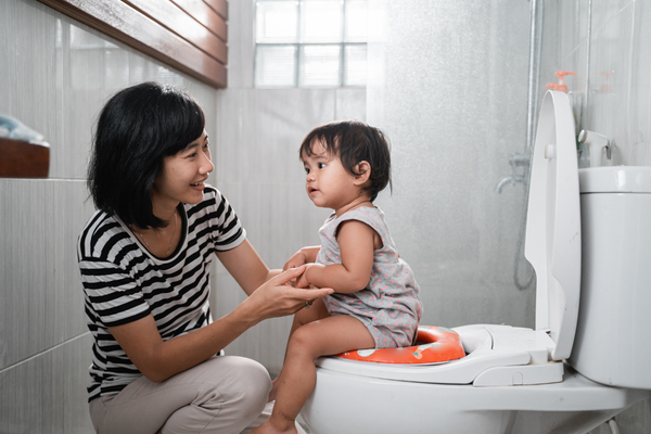 Toddler sitting on toilet with mother holding her