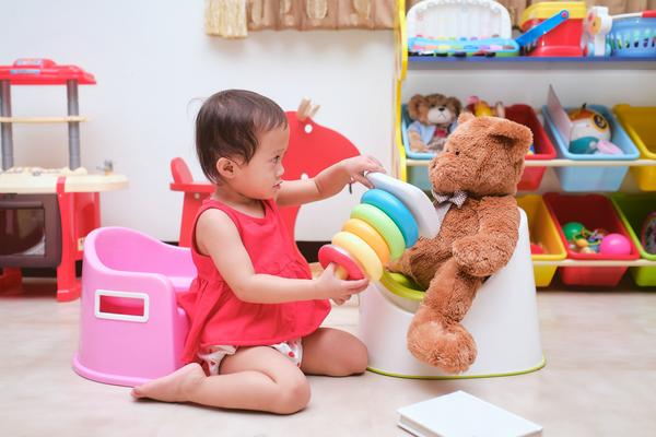Girl playing with toy bear who is seated on a potty