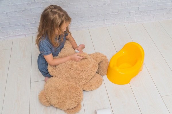 Girl sitting next to a potty holding a teddy bear
