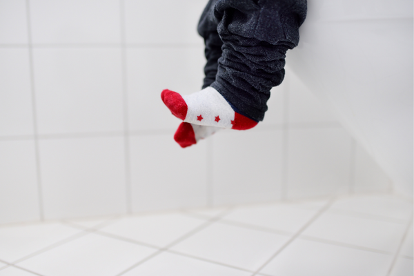 Child's feet dangling whilst sitting on a toilet. Child is wearing red and white socks.