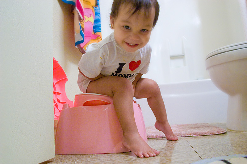 Toddler sitting on a pink potty in a bathroom smiling