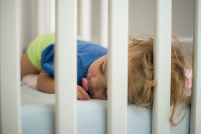 Toddler sleeping in cot with a pacifier