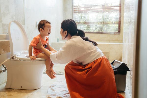Mother comforting boy sitting on toilet potty training